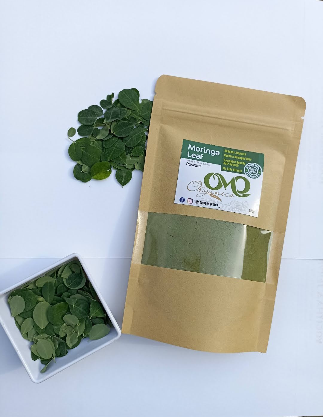 OhMyOrganics Moringa Leaves Powder pack with fresh moringa leaves displayed on a white background.